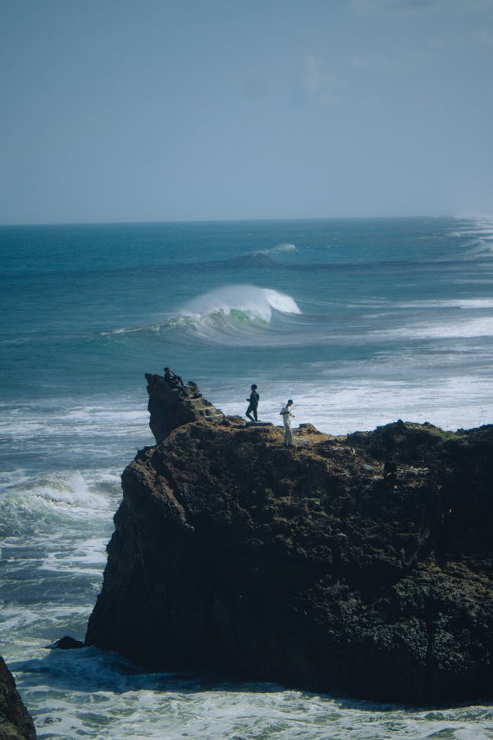 embark Two people stand on a dramatic cliff overlooking the ocean at Tasikmalaya, Indonesia.