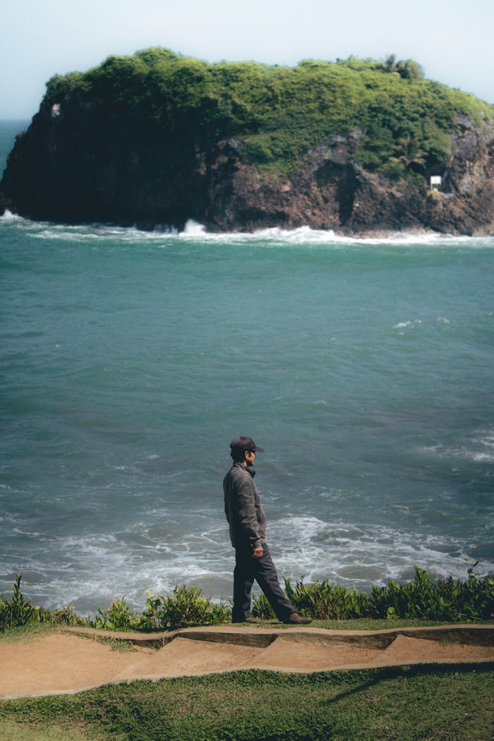 A man enjoys a tranquil moment by the ocean in Tasikmalaya, Indonesia, with lush greenery and calm waters.